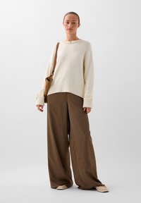 Cremefarvet strikket sweater med rund hals, kombineret med brune vidde bukser med en subtil tekstur og mønster.