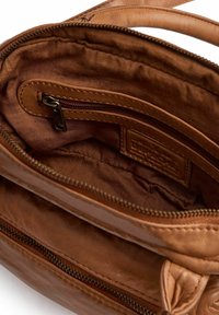 Interno di una borsa a tracolla in pelle marrone con un morbido rivestimento in tessuto, una tasca con zip e una sottile etichetta con il logo. La zip è dotata di un'utilizzo in metallo.