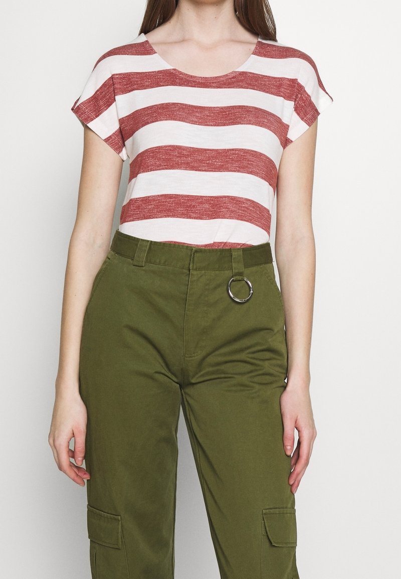 Top de manga corta a rayas rojas y blancas con escote redondo, combinado con pantalones cargo verdes ajustados que tienen un acento de anillo plateado en la cintura.