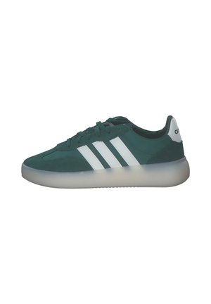 Zielony but sportowy Adidas z białymi potrójnymi paskami, przezroczystą podeszwą, zapięciem na sznurowadła i logo na języku z tyłu, widok z boku.