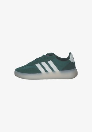 Zielony but sportowy Adidas z białymi potrójnymi paskami, przezroczystą podeszwą, zapięciem na sznurowadła i logo na języku z tyłu, widok z boku.