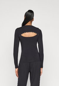 Melnas garo piedurkņu krekls ar viļņotu izgriezumu mugurpusē, izgatavots no mīkstas, elastīgas auduma. Gluda tekstūra un pieguļoša forma.