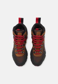 Botas de senderismo de ante marrón y malla negra con cordones rojos, ojales reforzados y una suela texturizada; incluye una cinta roja en el talón.