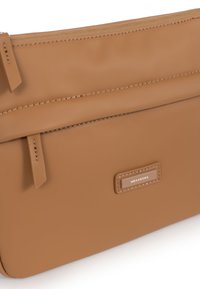 Borsa crossbody in finta pelle marrone con chiusura a zip, tasca piatta anteriore e patch con logo impresso. Texture liscia con cuciture minime.