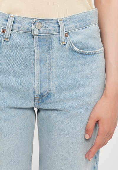 Light blue denim jeans feature a high waist, five-pocket design, and visible stitching. The fabric has a slightly faded texture.