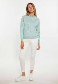 Felpa con cappuccio di colore azzurro chiaro con una finitura testurizzata, con cordini e polsini a costine, abbinata a pantaloni bianchi slim-fit e sneakers bianche.