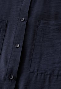 Camicia blu navy button-up in tessuto leggero con superficie testurizzata, due tasche frontali e cinque bottoni neri lungo la pattina.