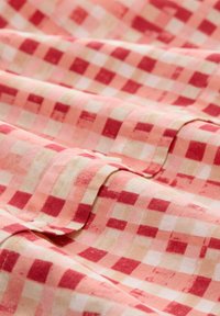 Tissu en coton à carreaux rouge et crème, présentant une texture froissée avec des motifs de carrés alternés et un drapé doux et fluide.