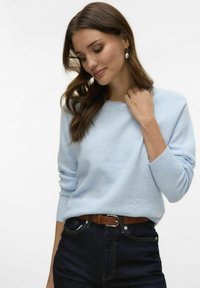 Heled sinine pehme kudumiga sviiter ümarate kaelustega ja ribikätistega, koos tumedate teksade ja pruuni nahkvööga.