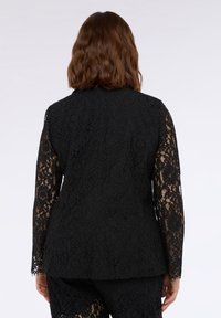 Blazer in pizzo nero con maniche lunghe caratterizzate da elaborati motivi floreali, scollatura rotonda e vestibilità strutturata. Tessuto delicato e testurizzato.
