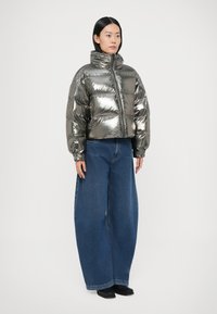 Izgriezta metāliski spīdīga pūkpūdera jaka ar augstu apkakli, kombinēta ar plašu kāju zilu džinsu biksēm un melniem apaviem. Gluda spoguļojoša tekstūra.