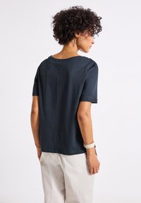 T-shirt à manches courtes bleu marine foncé avec un col rond et une coupe droite. Texture douce avec un détail de couture centrale au dos.