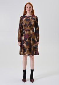 Een jurk met een bruine en paarse bloemenprint, lange mouwen, een aansluitende corsage en een uitlopende rok; gedragen met zwarte sokken en puntige schoenen.