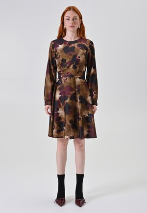 Een jurk met een bruine en paarse bloemenprint, lange mouwen, een aansluitende corsage en een uitlopende rok; gedragen met zwarte sokken en puntige schoenen.