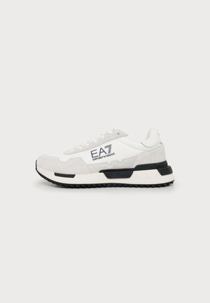 Zapatilla Emporio Armani EA7 blanca y gris claro con detalles negros en la suela y branding en el lateral, mostrada sobre un fondo liso.