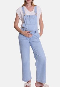 Lichtblauwe denimschorten met wijde pijpen, verstelbare schouderbanden, een voorklep en een ontspannen pasvorm, gecombineerd met een witte V-hals top.