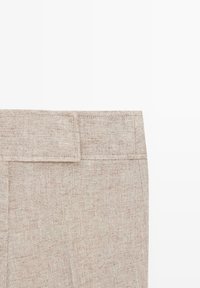 Beige linen trousers waist area with belt loops and side seam visible on a white background.