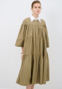 Abito in cotone verde oliva con colletto bianco a scollatura ondulata, design a strati, maniche a mezzo busto e dettagli arricciati.