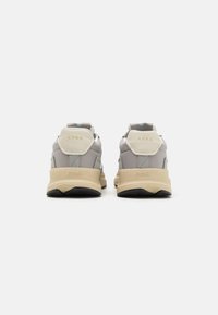 Et par grå og beige ARKK-sko sett fra baksiden, som viser tykke beige såler og "ARKK"-merking på hæltabbene.