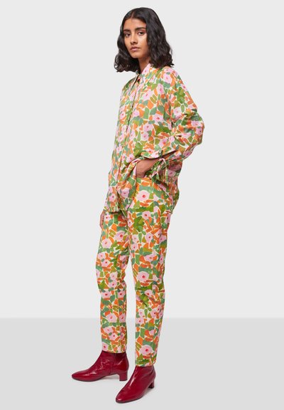 Completo a fiori nei colori verde, rosa e arancione; camicia morbida e pantaloni a gamba dritta. Il modello indossa stivaletti alla caviglia rossi e lucenti.