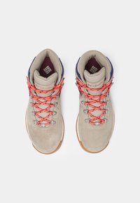 Bottes de randonnée beiges avec des lacets orange, des collerettes rembourrées, des œillets métalliques et des logos de la marque Columbia à l'intérieur et sur la languette, vues de dessus.