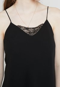 Camisole nera con sottili spalline, caratterizzata da una scollatura a V e un inserto in pizzo sul petto. Realizzata in un tessuto morbido e leggero.