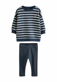 Sudadera a rayas azul marino y crema con puños y cuello de canalé; presenta un pequeño bordado de un coche naranja. Combinada con leggins de canalé azul marino.