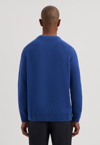 Sininen neulepaita, jossa on teksturoitu kuvio, resorit hihansuissa ja helmassa sekä pyöreä pääntie. Takakuvassa näkyvät saumatonta raglan-hihat.