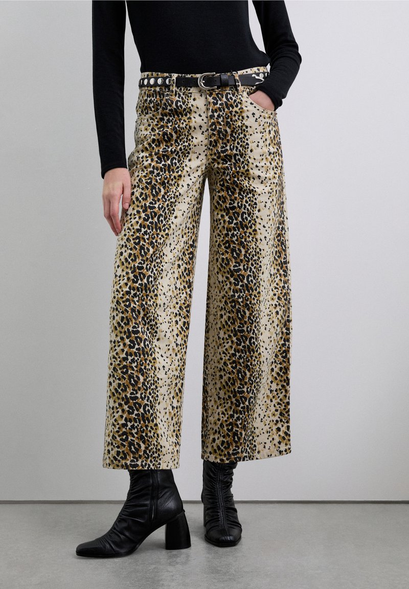 Pantalon large à imprimé léopard sur fond crème, avec une ceinture noire ornée d'une boucle en métal argenté. La texture est lisse avec des motifs distincts.