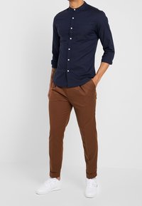 Mörkblå långärmad skjorta med knappknäppning och krage, matchad med bruna chinos och vita sneakers, med en enda bröstficka.