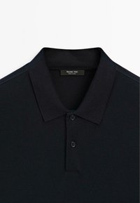 Schwarzes Poloshirt mit kurzen Ärmeln, zwei Knöpfen und Kragen, mit einem "Massimo Dutti"-Etikett im Nacken.