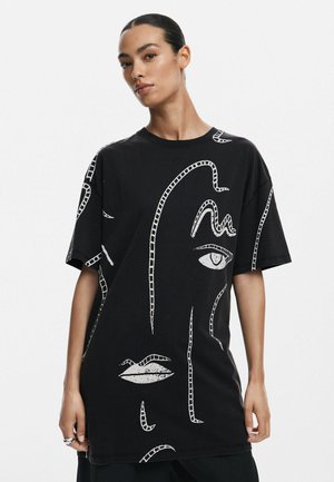 Sort oversized t-shirt lavet af bomuld, med hvide abstrakte ansigtsdesigns, herunder øjne og læber. Korte ærmer, rund halsudskæring.