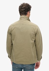 Licht olijfgroene katoenen jas met een verhoogde kraag, knoopmanchetten en een rechte zoom. Glad textuur en casual pasvorm.