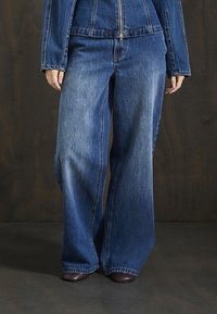 Jeans de mezclilla de tiro alto en un tono azul claro, con pernera ancha y un diseño ligeramente deslavado. La tela tiene una textura suave y detalles de costura.