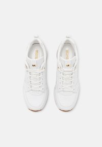 Chaussures de sport blanches avec une tige en cuir lisse, fermeture à lacets, col matelassé et accents de logo dorés. Semelle extérieure en caoutchouc avec adhérence texturée.