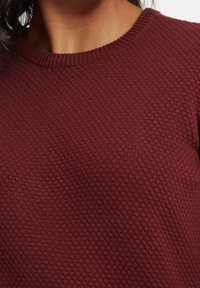 Bordowy sweter dzianinowy z okrągłym dekoltem, z teksturowanym wzorem plastra miodu. Gładki materiał z prążkowanymi detalami przy kołnierzu.