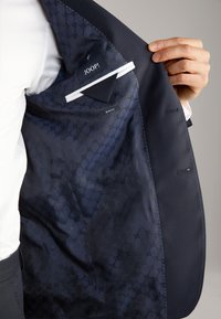 Wnętrze marynarki w kolorze granatowym z wzorzystą podszewką, z metką "JOOP!" i kieszonką. Widoczna metka slim fit w dolnej części.