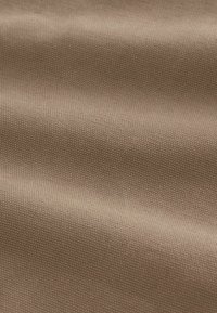 Tissu tissé brun clair avec une texture en fine grille et des plis doux et délicats créant des ombres subtiles.