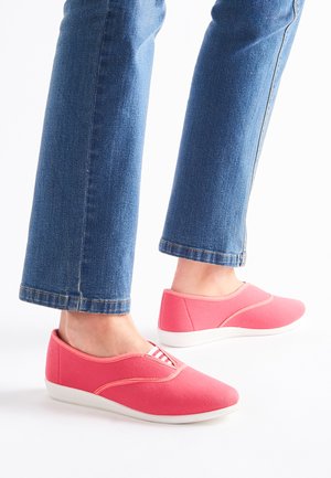 Rosa Slipper aus strukturiertem Stoff, mit einer weißen Sohle und dezenten kontrastierenden Nähten, kombiniert mit blauen Jeans.