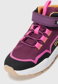 Paarse en roze sportschoen met een zwarte teenkap, witte zool, roze trekband en gele binnenvoering.