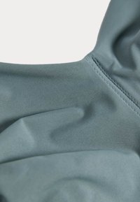 Blågrön tyg med en jämn, något stretchig textur. Har en rundad söm för formning och en ren finish längs kanterna.