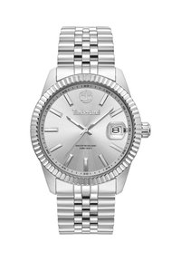 Reloj de acero inoxidable plateado con un dial texturizado, marcadores de hora luminosos, indicador de fecha y un bisel estriado. Resistente al agua hasta 50 m.