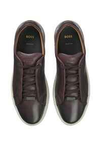 Sneakers in pelle BOSS di colore bordeaux scuro con punta tondeggiante, lacci ton sur ton, suola bianca a contrasto e logo in rilievo sulla linguetta.