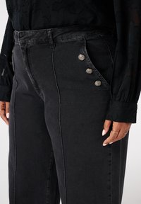 Zwarte denim broek met een hoge taille, zijknopen en contrasterende stiksels. Glad materiaal met een relaxte pasvorm.