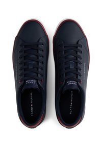 Paire de baskets Tommy Hilfiger bleu marine avec lacets noirs et bordure rouge foncé, vue de dessus sur fond blanc.