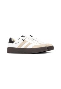 Zapatillas blancas con acentos de ante gris y beige. Presenta un talón y un logotipo negros, cordones planos y una suela de goma oscura y gruesa. Diseño atlético clásico.