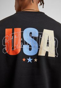 Čierna mikina s preležaným logom "USA" v červenej, modrej a krémovej farbe, s tromi hviezdami pod logom v červenej, modrej a béžovej farbe. Vyrobená z bavlny.