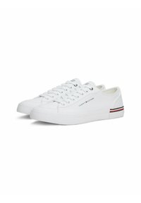 Zapatillas de lona blancas con un perfil bajo, punta redonda y diseño de cordones. Presentan texto de marca en el lateral y un acento a rayas en el talón.