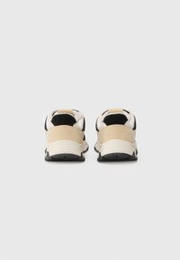 Sko som har en svart og kremfarget overdels med semsket skinn og mesh-materialer, svarte såler og en myk beige hæltab.