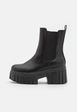 Bottine noire en cuir avec semelle épaisse à plateforme striée et panneau latéral élastique, dotée d'une languette à l’arrière.